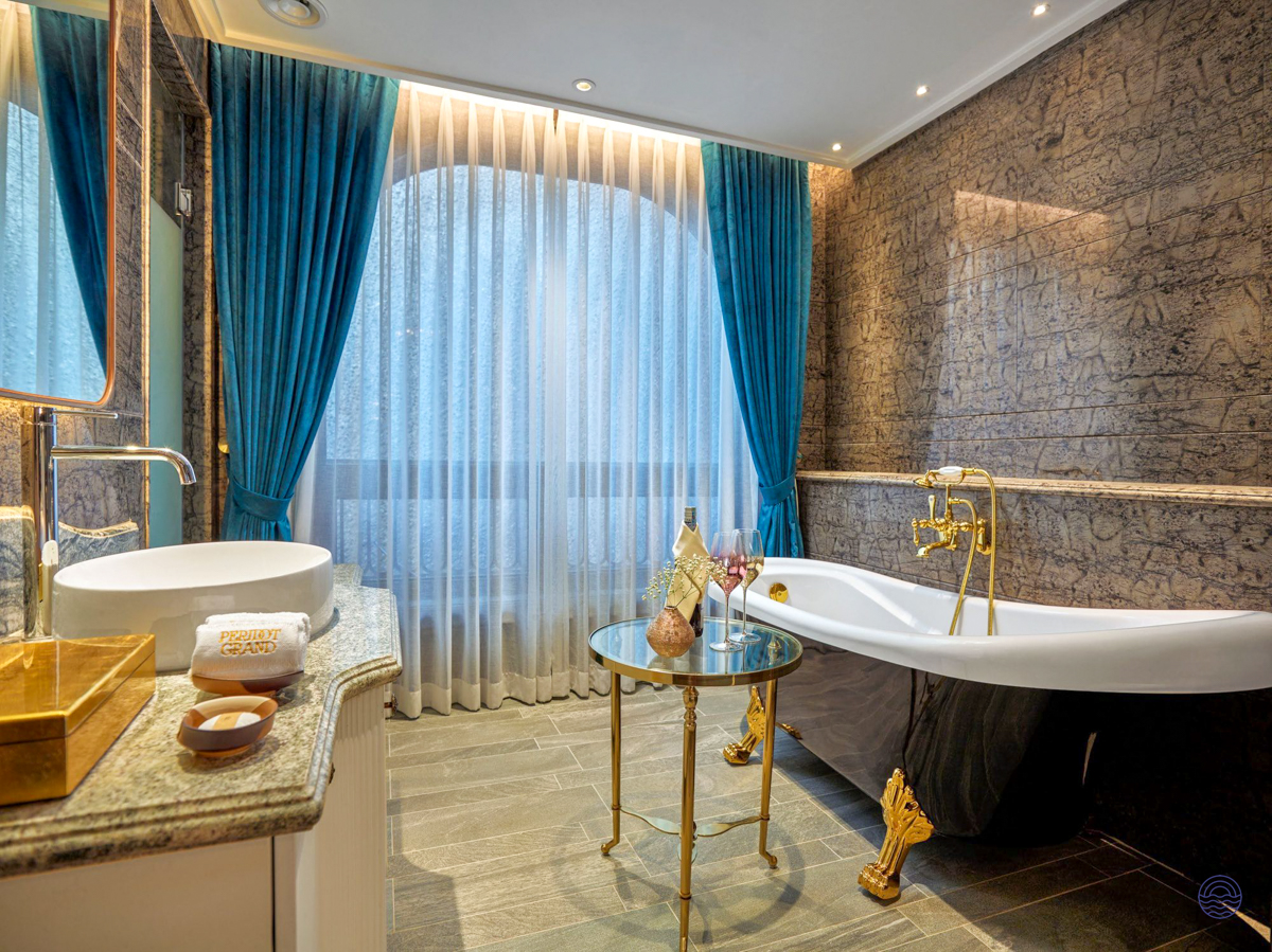Luxurious bathroom with a freestanding tub, gold fixtures, and blue curtains at the Peridot Grand Hotel, Hanoi.