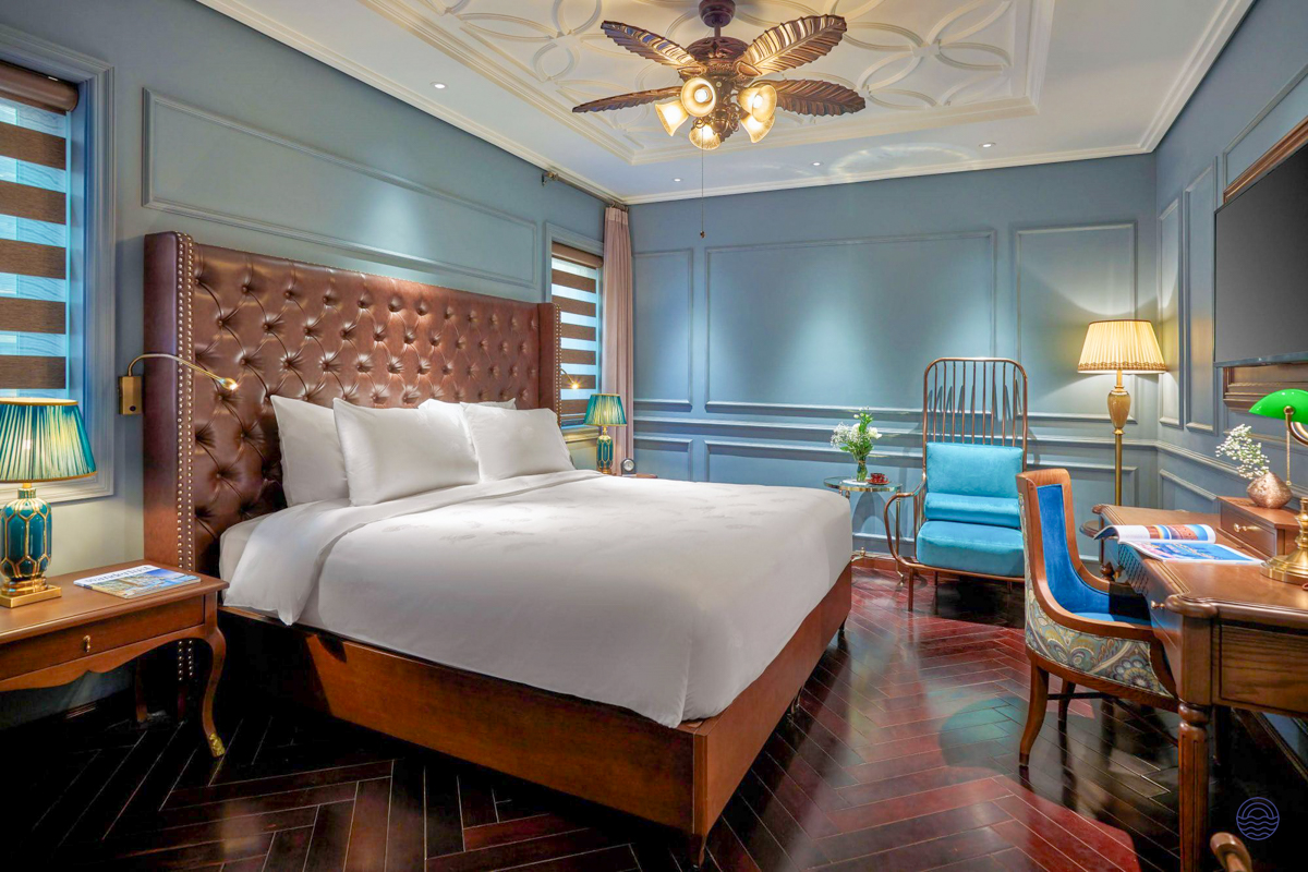 Elegant hotel room in Hanoi featuring a large bed, blue walls, and a stylish desk area.