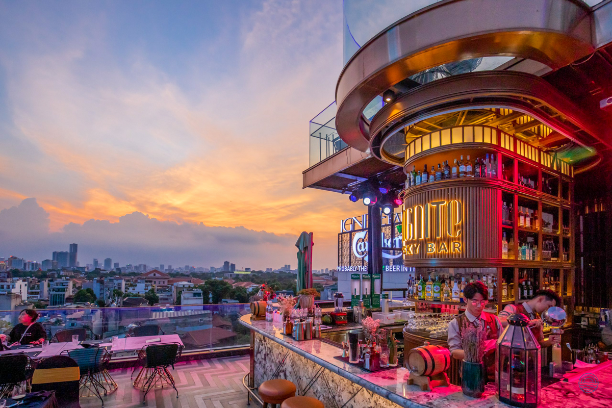 A vibrant rooftop bar in Hanoi with guests enjoying drinks and a beautiful sunset city view.