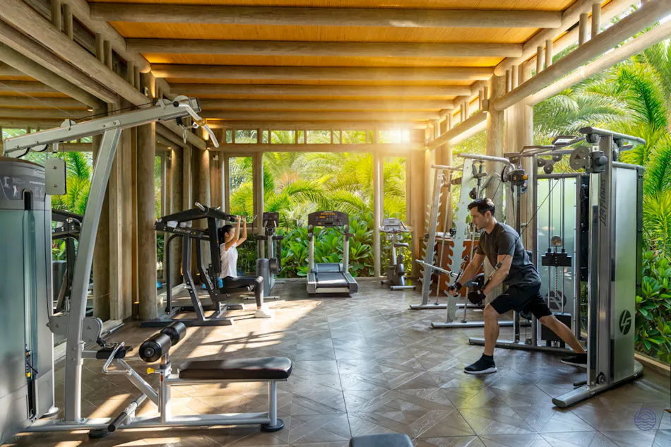 Two people exercising in a modern gym with tropical views at An Lam Retreats Saigon River.