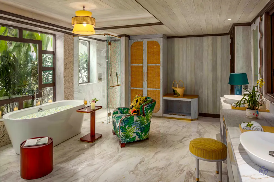 Luxurious bathroom with a large soaking tub, tropical armchair, and lush green outdoor view.