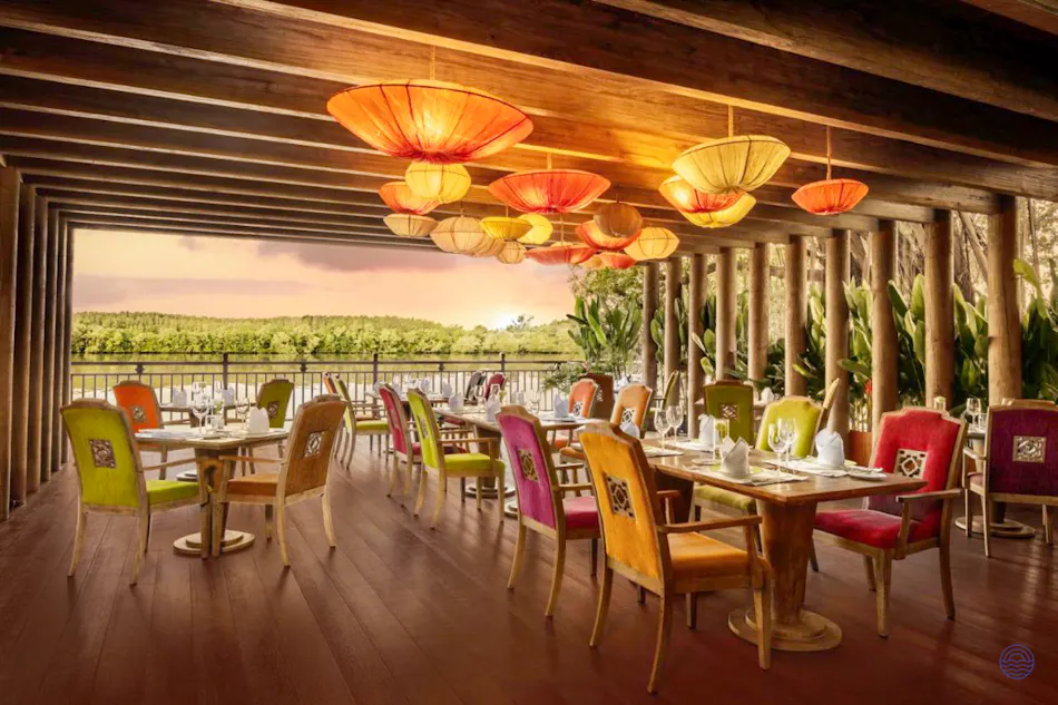 Colorful lanterns illuminate an elegant open-air restaurant overlooking the Saigon River at sunset.