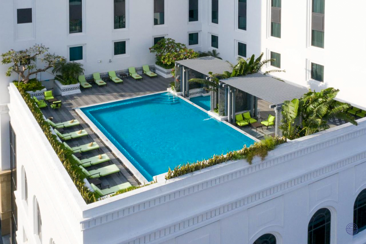 Modern rooftop swimming pool with green lounge chairs at Mai House Saigon Hotel in Ho Chi Minh.