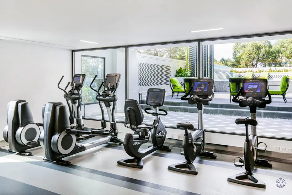 A bright, modern hotel gym with various exercise machines and a view of an outdoor patio.