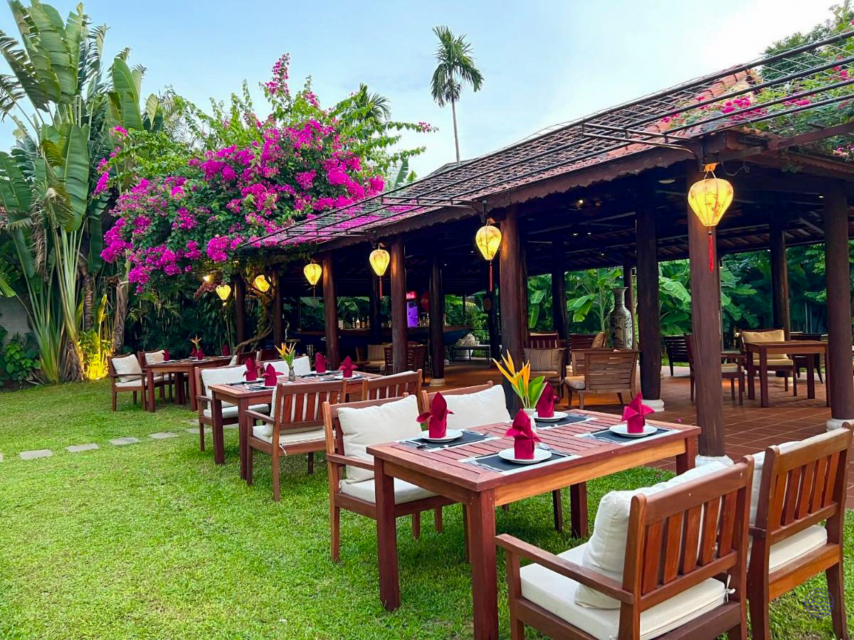 Lush outdoor dining area with wooden tables, lanterns, and vibrant pink bougainvillea in Hoi An.