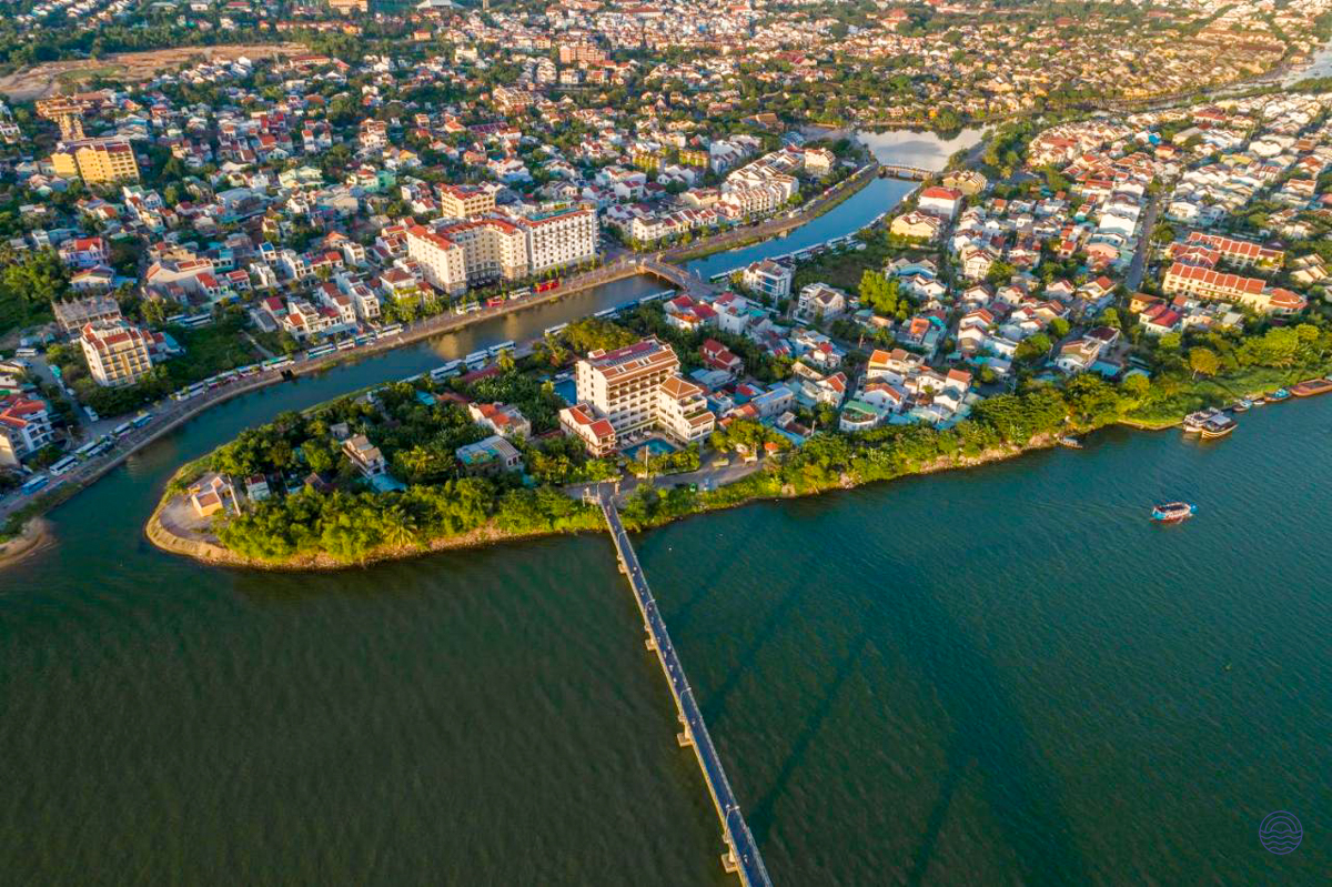 An aerial view captures the vibrant riverside city of Hoi An, Vietnam, with a long bridge.