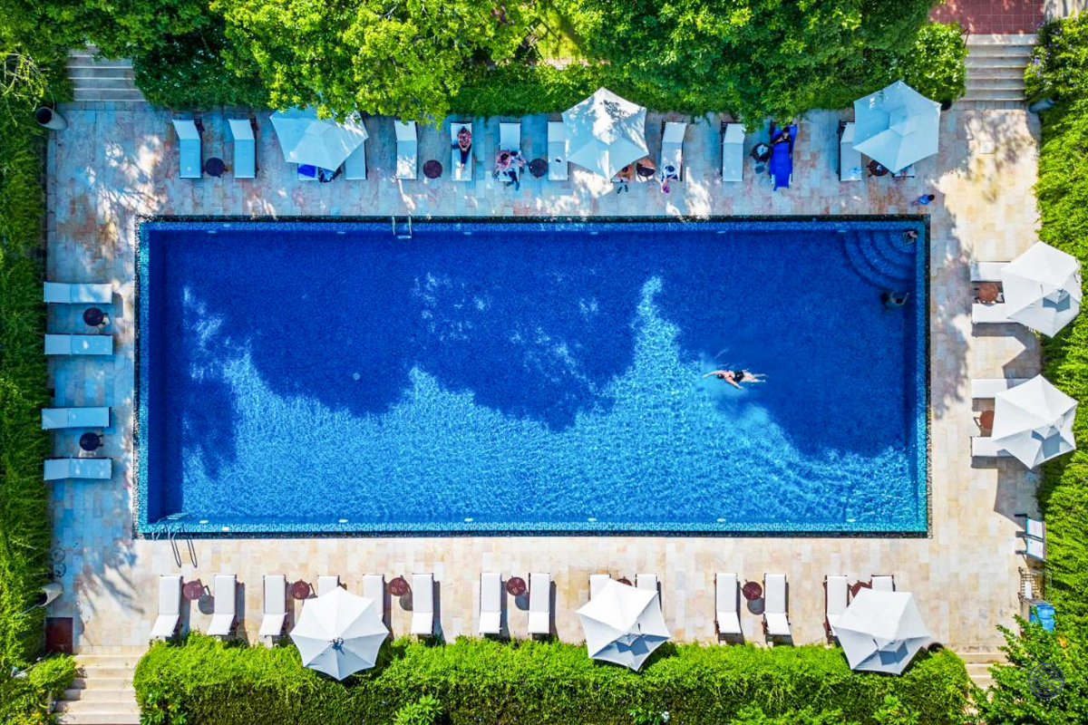 Aerial view of a vibrant blue swimming pool surrounded by sun loungers and green foliage in Hoi An.