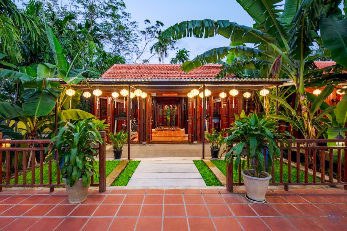 A charming traditional guesthouse in Hoi An, beautifully lit by warm lanterns amidst lush tropical plants.
