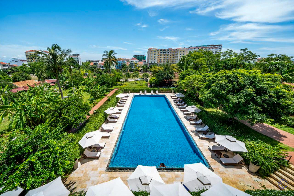 A long, sparkling blue swimming pool surrounded by lounge chairs and lush tropical gardens in Hoi An.