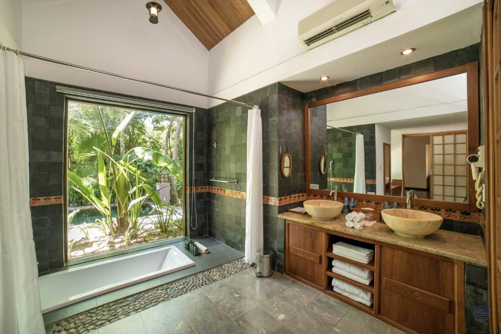 Serene bathroom at Pilgrimage Village Hue, boasting a deep soaking tub and lush private garden.