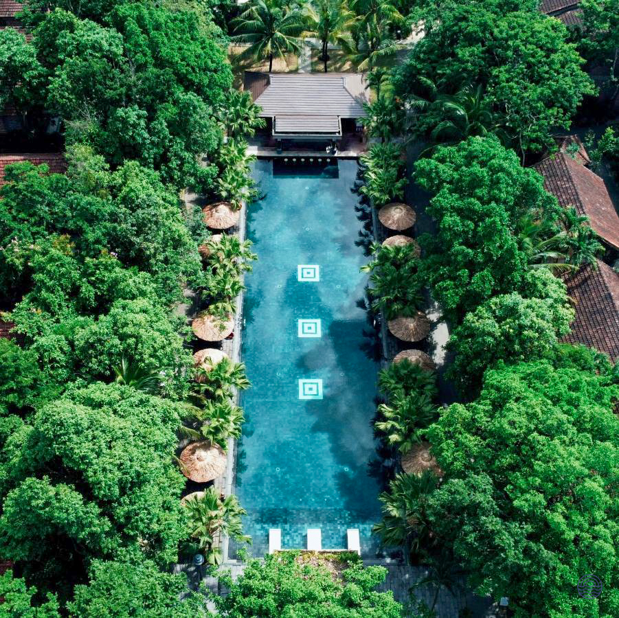 A tranquil resort swimming pool in Hue, nestled among lush tropical gardens with sun umbrellas.