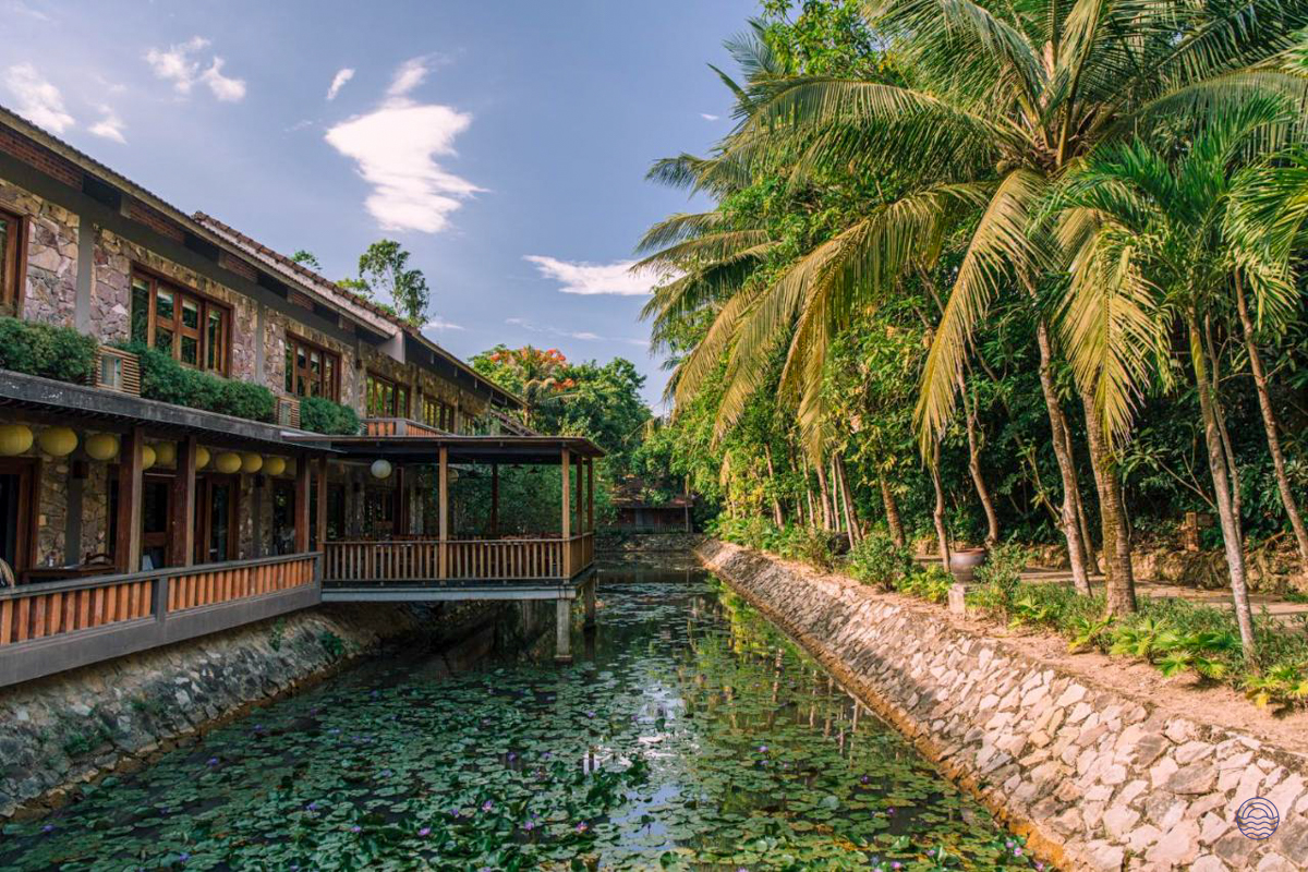 Pilgrimage Village Boutique Resort in Hue, featuring lush tropical gardens and a peaceful canal.