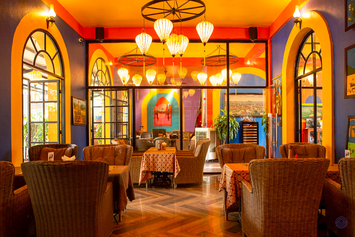 A vibrant and colorful cafe interior with wicker chairs, arched windows, and unique hanging lanterns in Phong Nha.