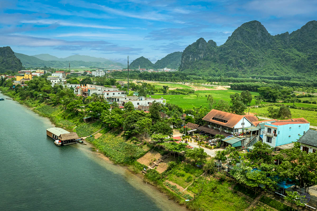 Scenic Phong Nha village along a tranquil river with lush green fields and dramatic karst mountains.