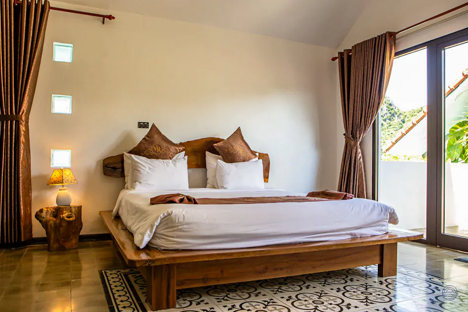 A bright and inviting bedroom in a Phong Nha villa, featuring a large wooden bed and balcony.