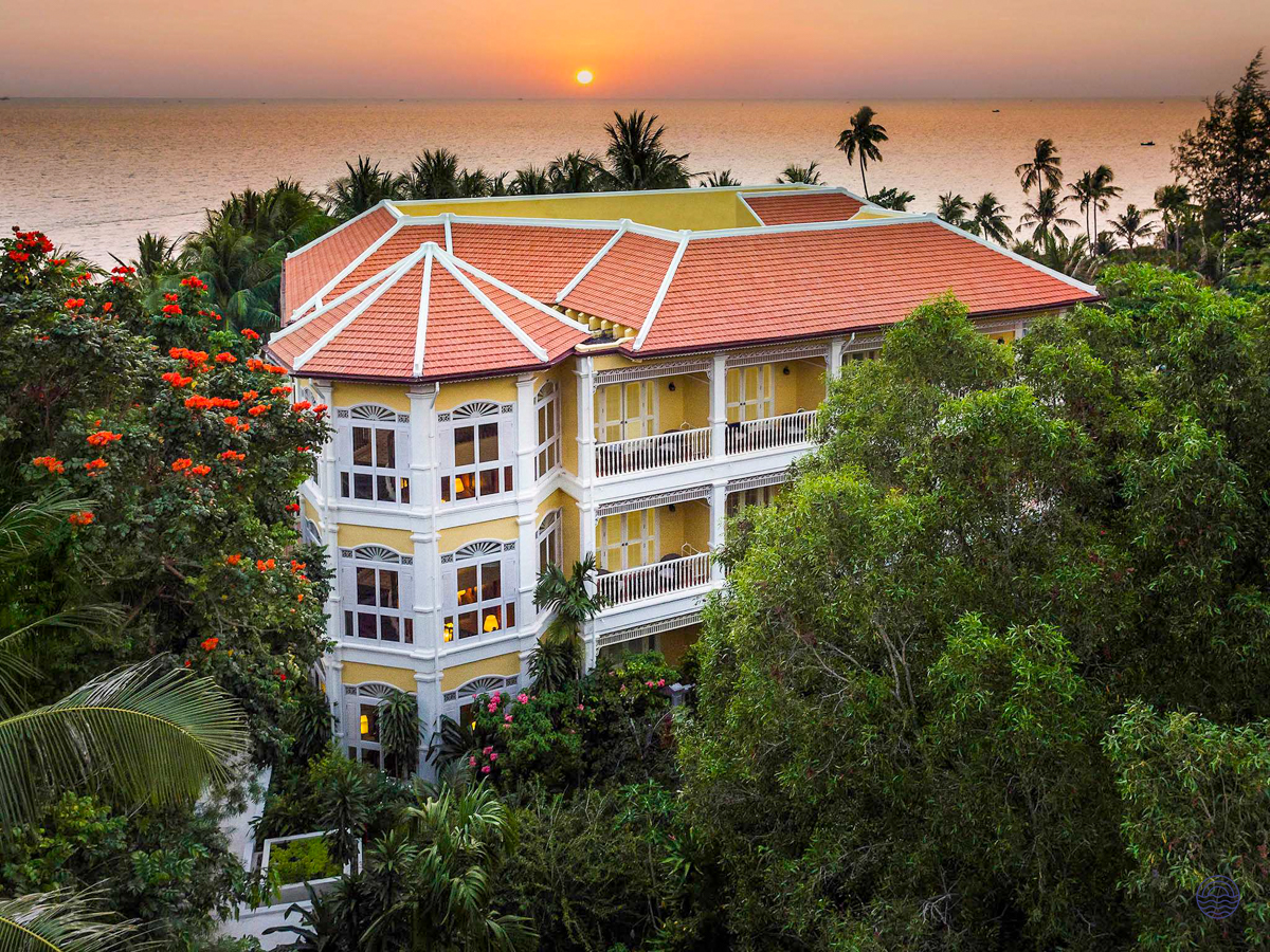 Elegant yellow resort building with red roof, tropical trees, and ocean sunset in Phu Quoc.