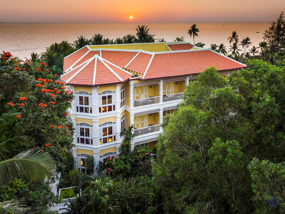 Elegant yellow resort building with red roof, tropical trees, and ocean sunset in Phu Quoc.