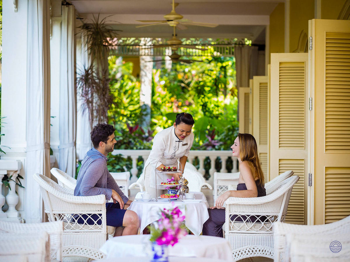 A smiling couple enjoys afternoon tea served by staff on a resort veranda in Phu Quoc.