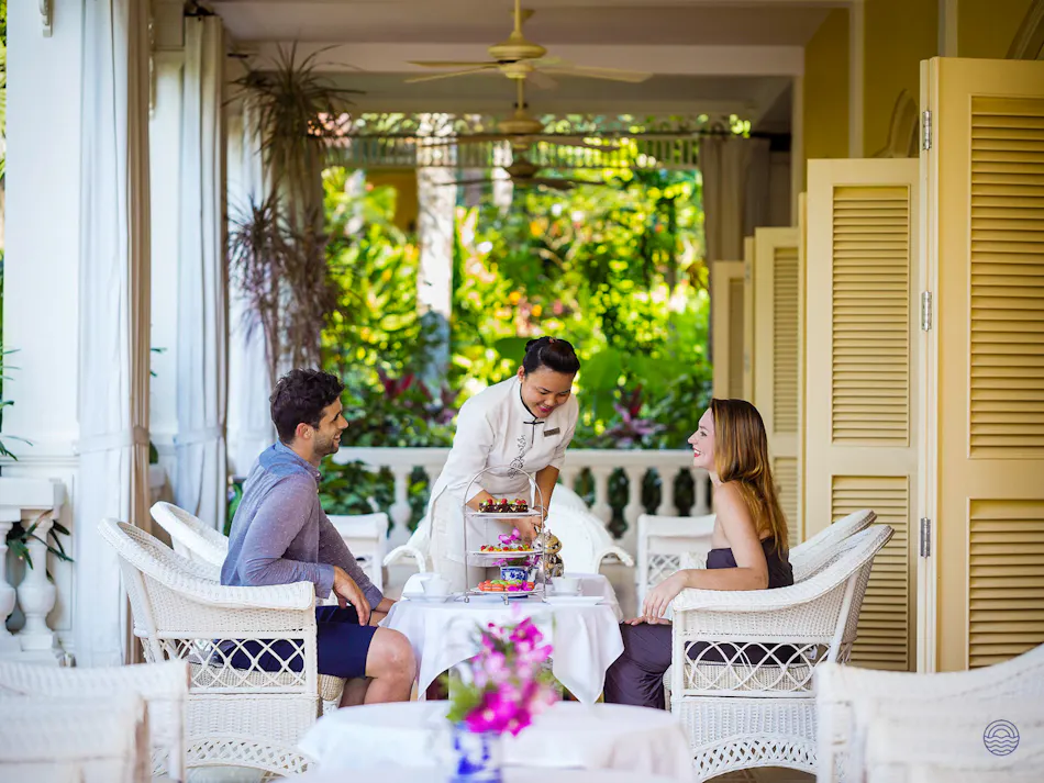 A smiling couple enjoys afternoon tea served by staff on a resort veranda in Phu Quoc.
