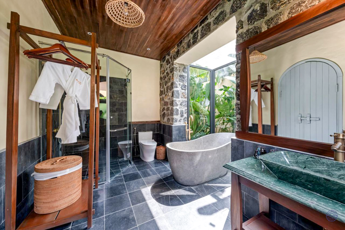 Luxurious bathroom at Tam Coc Retreat with stone tub, green sink, and tropical garden views.