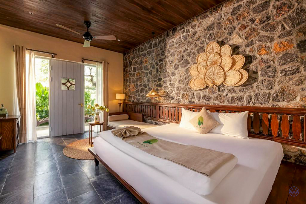 A tranquil room at Tam Coc Retreat with a large bed, stone wall, and garden view.