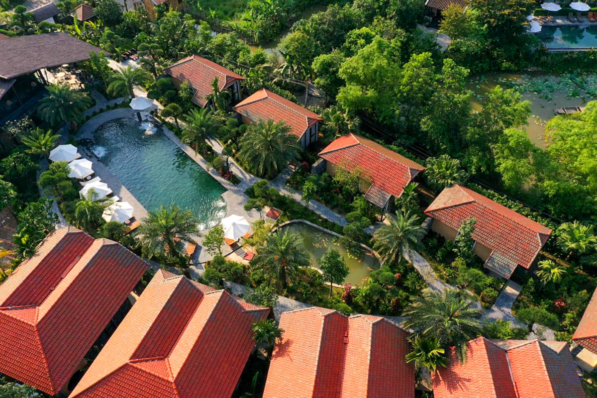 Tranquil Tam Coc Retreat with red-roofed buildings, a swimming pool, and lush green tropical gardens.