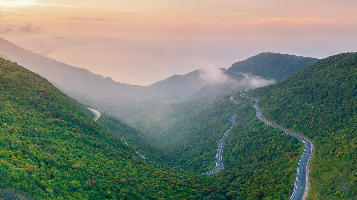 Winding road through lush green mountains of Hai Van Pass under a soft, hazy sky.