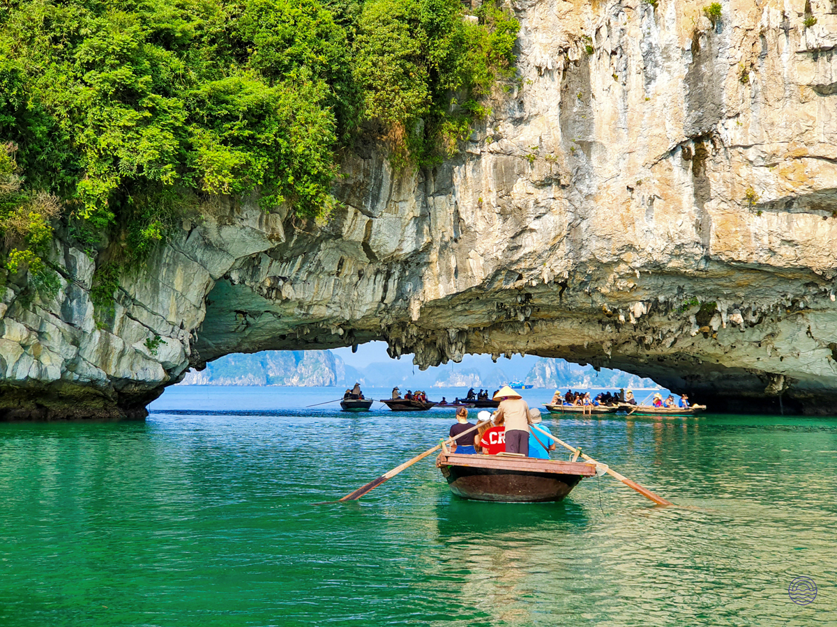 Tourists in traditional boats navigate through a magnificent rock archway on the emerald waters of Tam Coc.