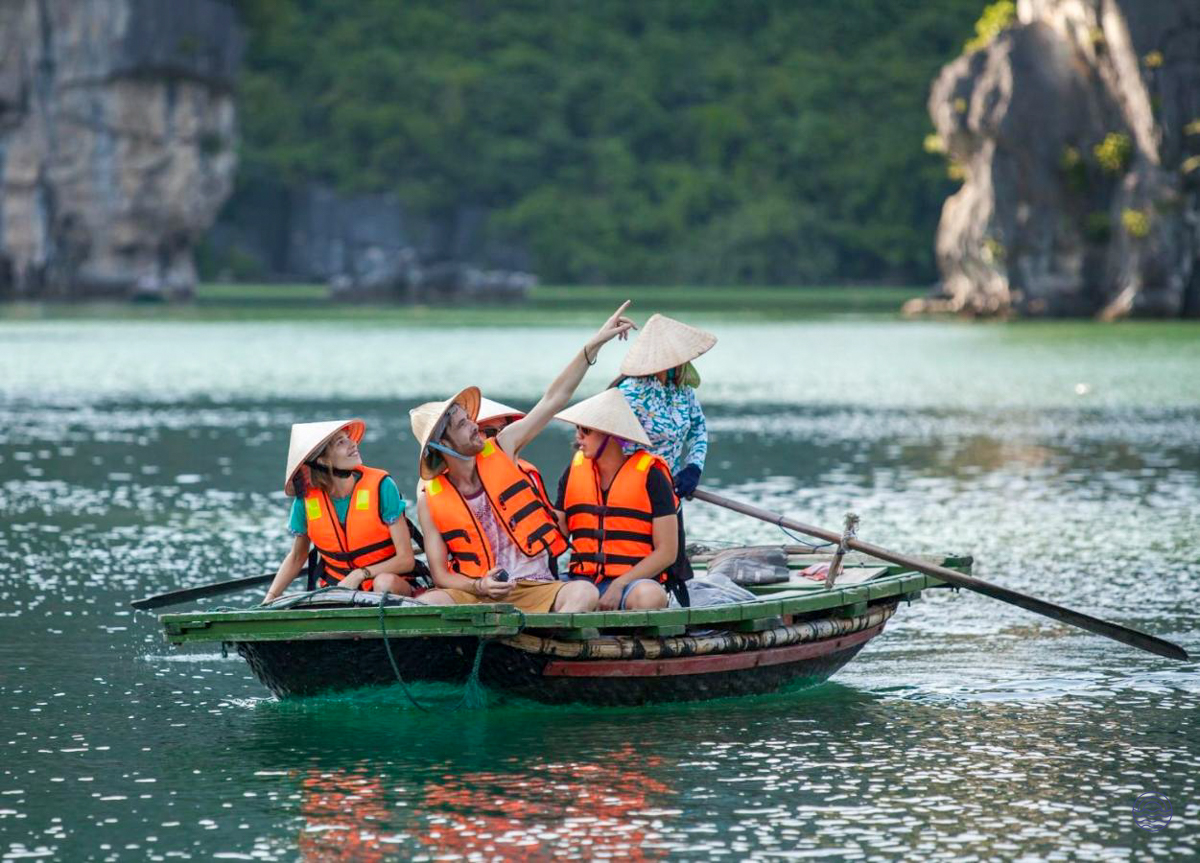 Tourists in life vests and conical hats on a boat, pointing at the scenic Tam Coc karsts.