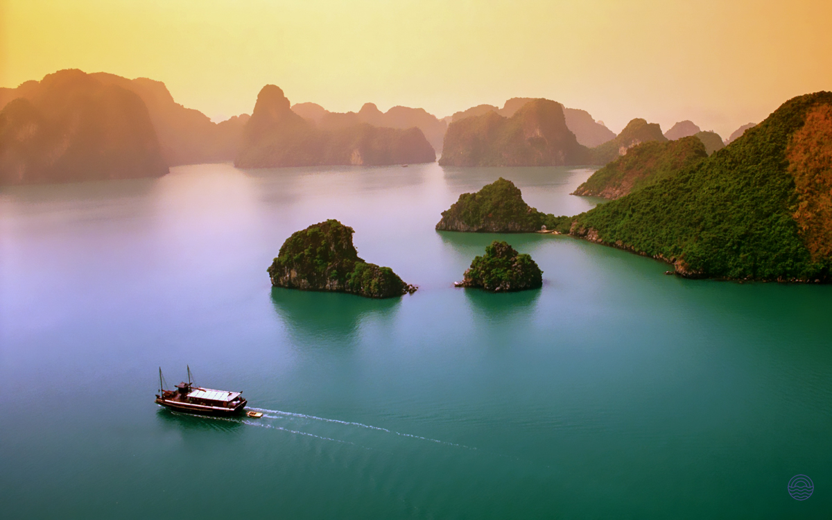 A traditional boat cruises through the emerald waters of Ha Long Bay, surrounded by majestic limestone karsts.