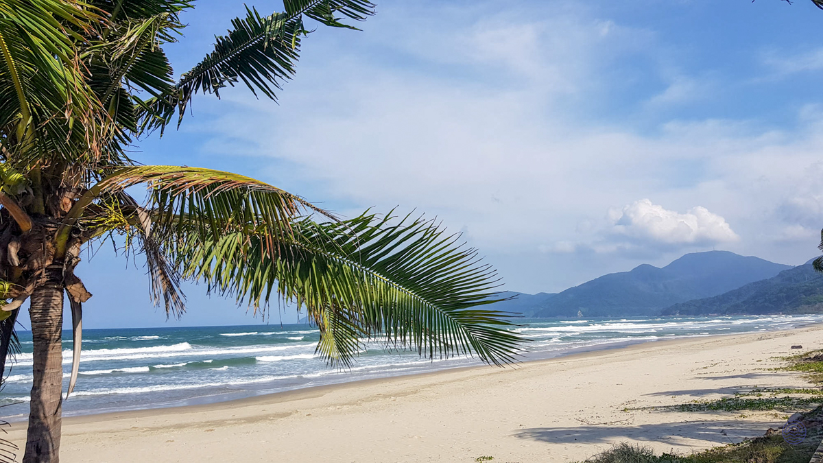 Scenic An Bang Beach in Hoi An, Vietnam, featuring golden sands, rolling waves, and distant mountains.