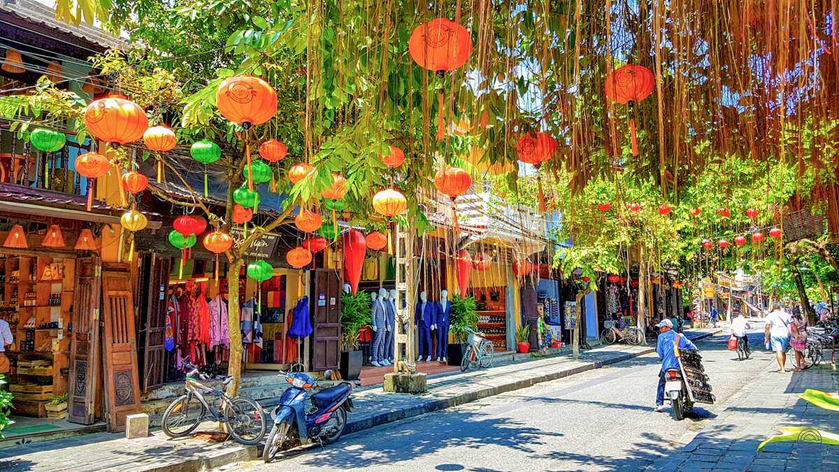 Vibrant lanterns and lush greenery adorn a bustling street in the charming town of Hoi An.