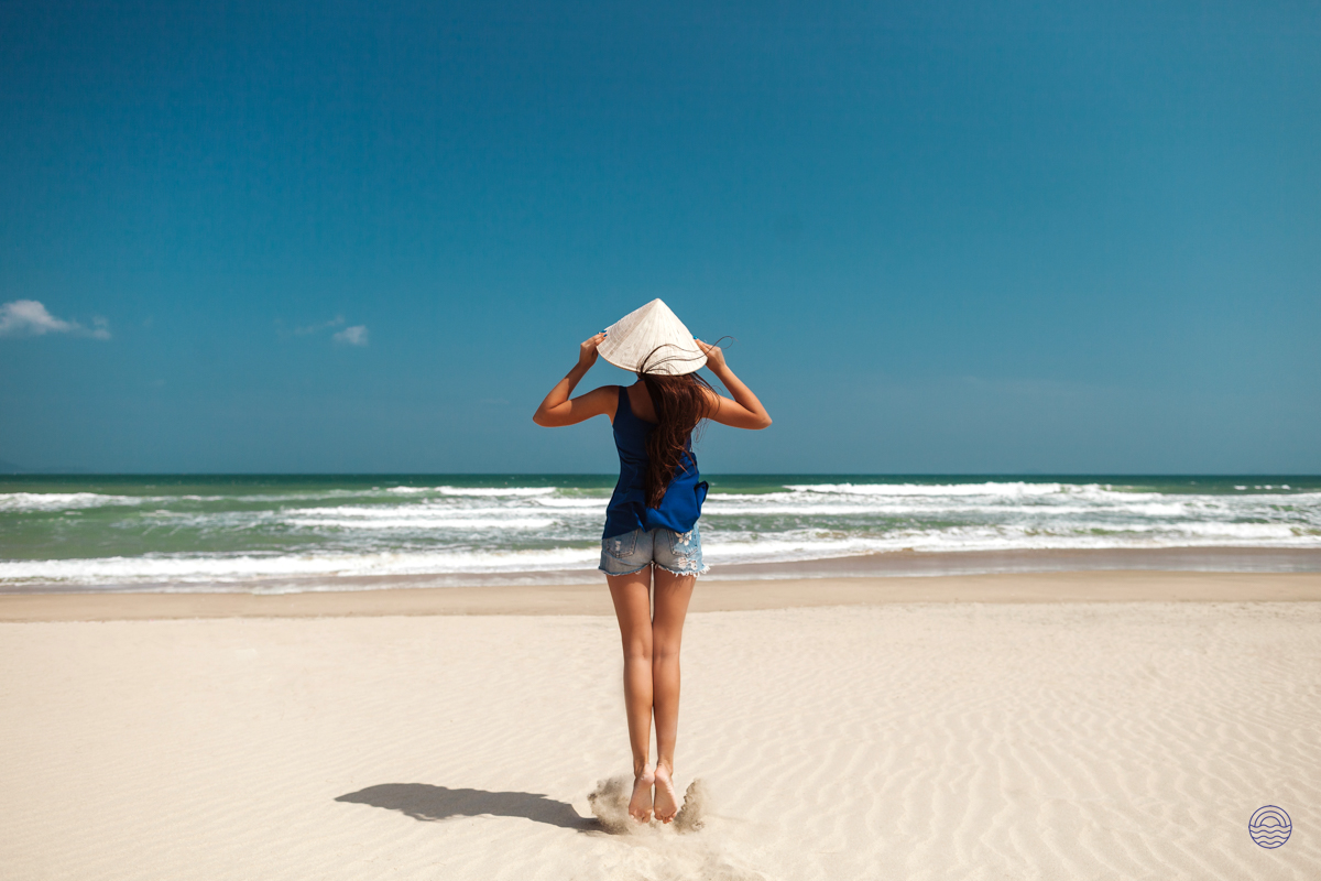 Woman in a conical hat enjoys the pristine white sands and clear blue ocean at Thuan An Beach.