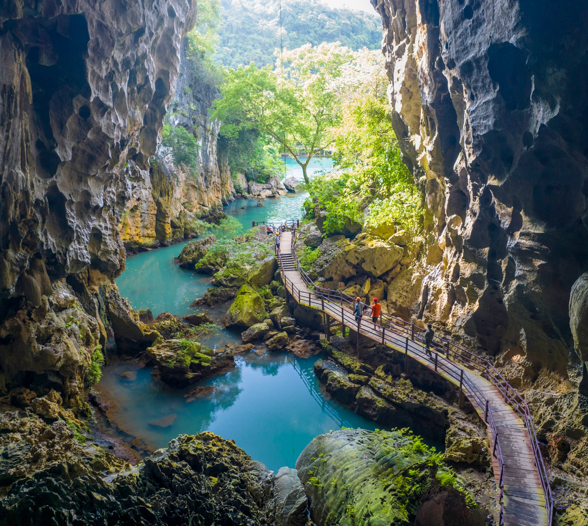 Visitors explore a stunning cave with a turquoise river and wooden walkway in Phong Nha.