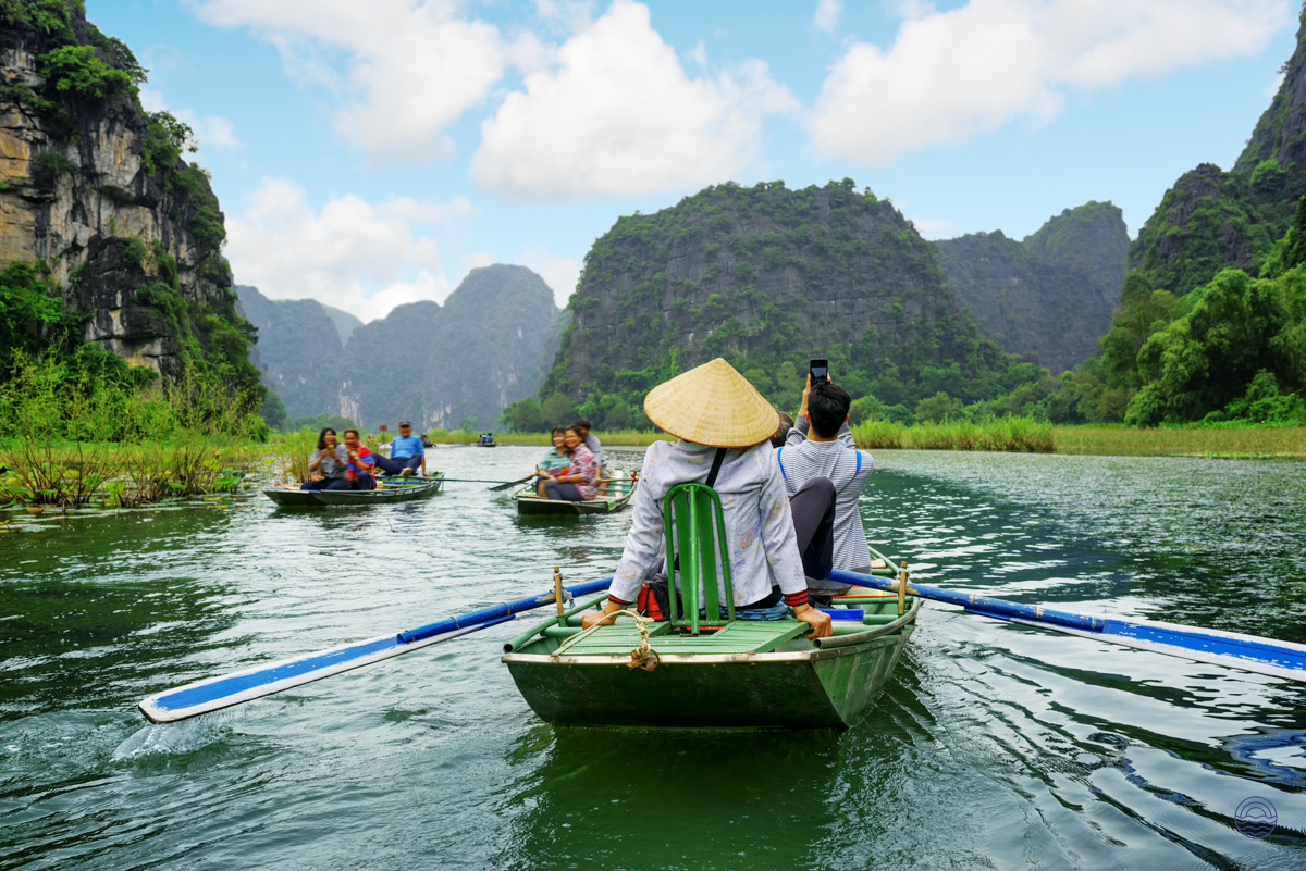 Visitors experience a tranquil sampan boat ride through Tam Coc's scenic waterways, framed by towering limestone karsts.