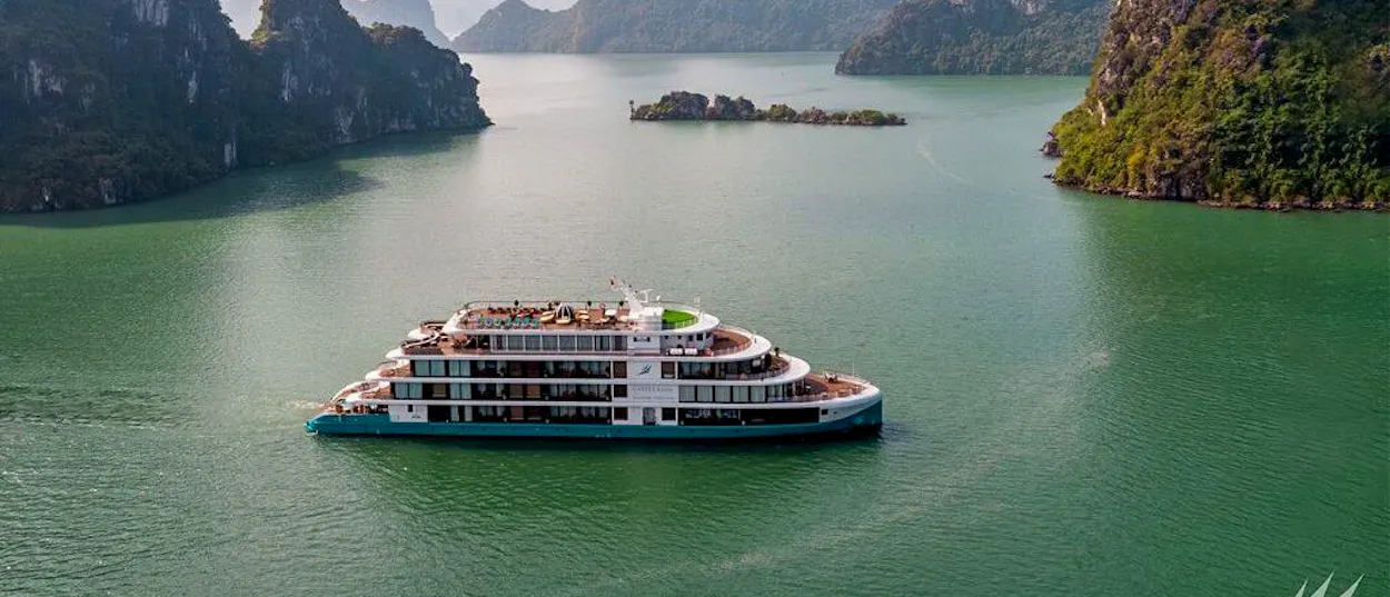 A large cruise ship sails through the emerald waters of Ha Long Bay, surrounded by towering limestone islands.