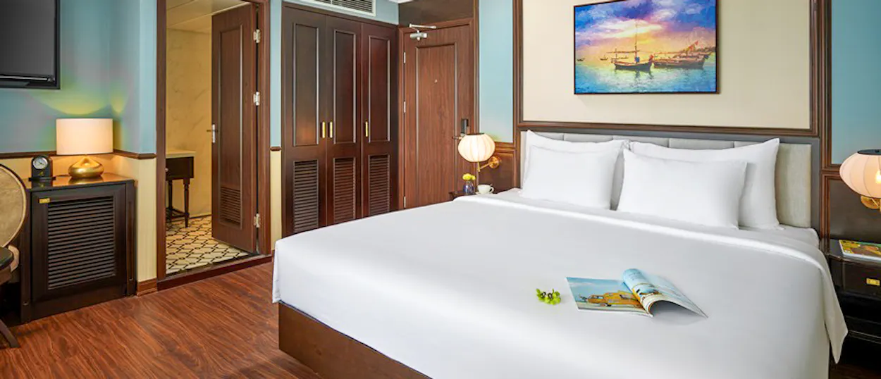 Inviting cruise cabin on Capella Cruise in Halong Bay with a large bed and wooden details.