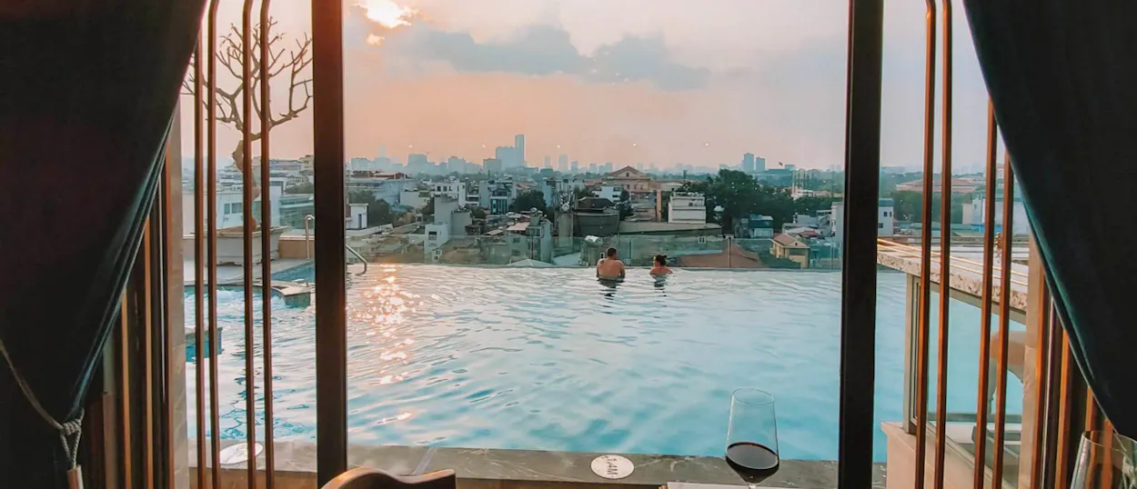 Two people relax in a rooftop infinity pool overlooking the Hanoi city skyline at sunset.