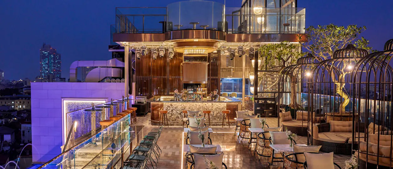 Luxurious rooftop bar in Hanoi with elegant seating, a glowing bar, and city views at night.