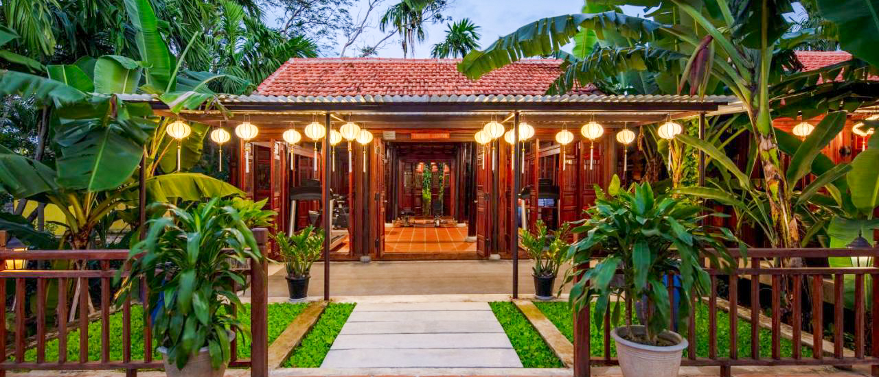 An inviting resort entrance in Hoi An, Vietnam, with glowing lanterns and lush tropical plants.