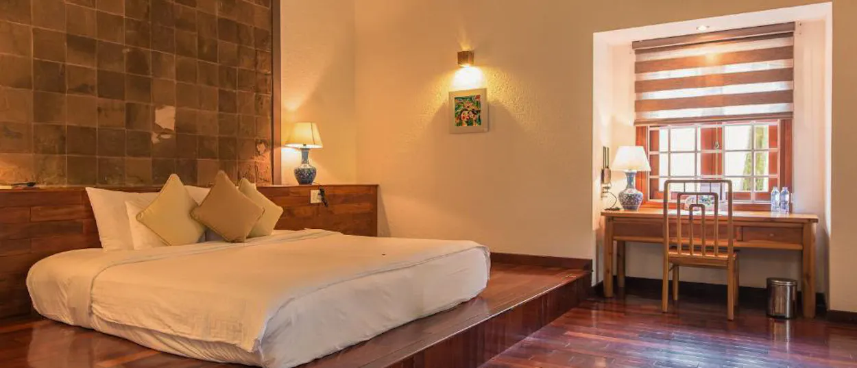 A spacious, warm-lit hotel room in Hue with a large bed and a wooden desk by a window.
