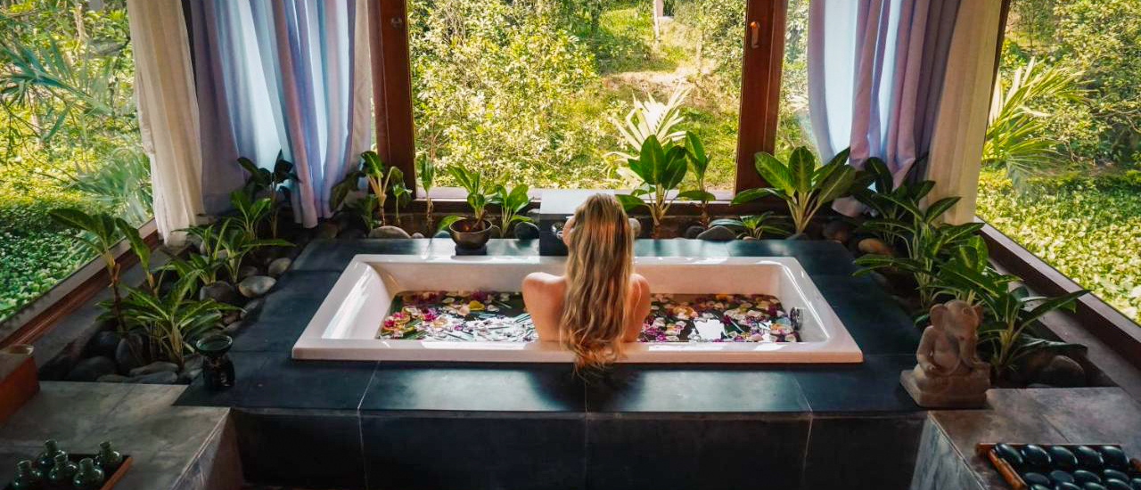 Blonde woman relaxing in a flower-filled bath overlooking a lush Vietnamese jungle.
