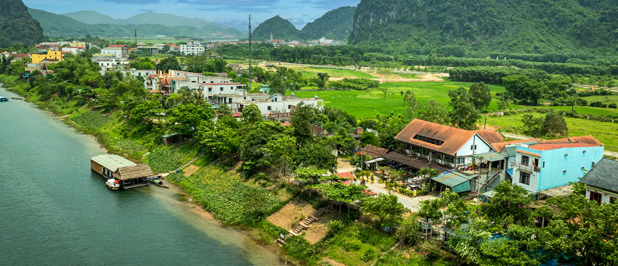 Serene riverside villas and green rice fields in Phong Nha, backed by lush, majestic mountains.