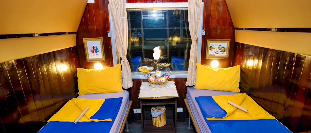 A cozy overnight train cabin with two beds, blue sheets, yellow pillows, and a window.