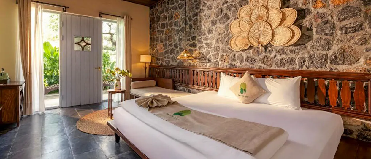 Tranquil bedroom at Tam Coc Retreat, featuring a stone wall, natural decor, and open door to gardens.