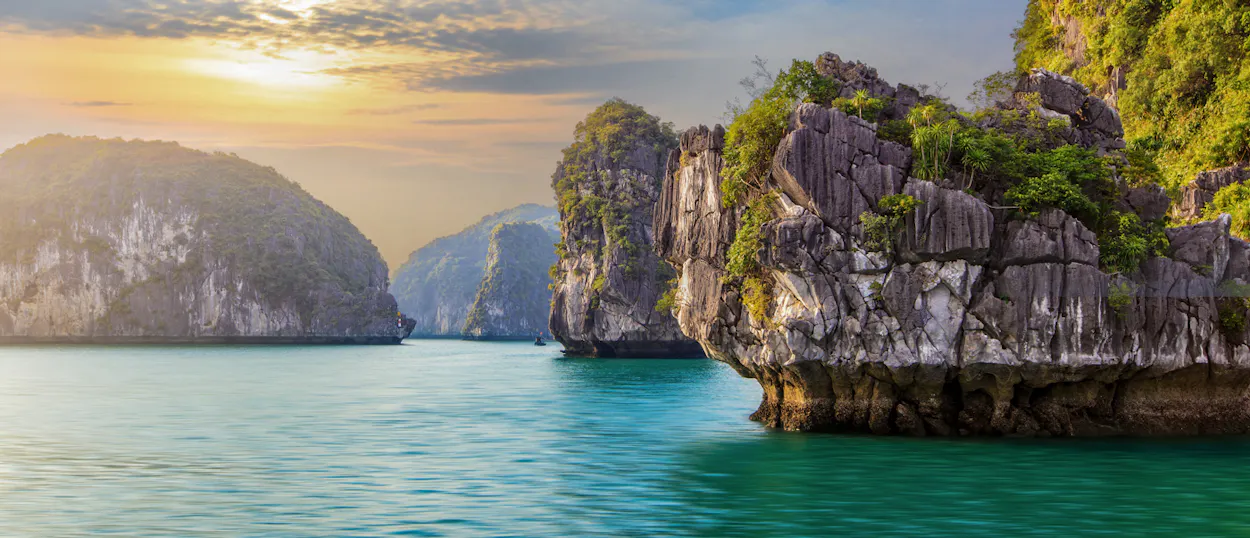 Majestic limestone karsts emerge from emerald waters under a glowing sky in Tam Coc, Vietnam.