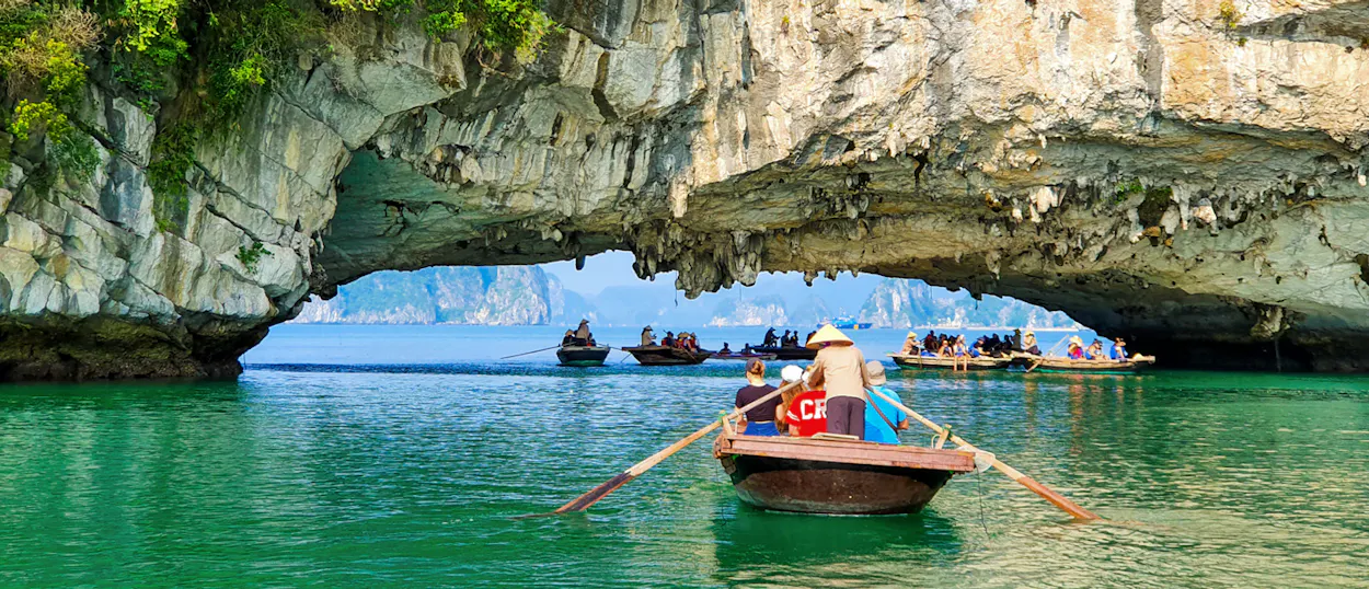 Boats with people in conical hats navigate through a stunning rock archway in Tam Coc, Vietnam.