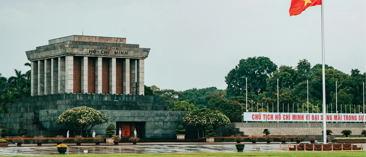 Guards stand before the imposing Ho Chi Minh Mausoleum in Hanoi on a cloudy day.