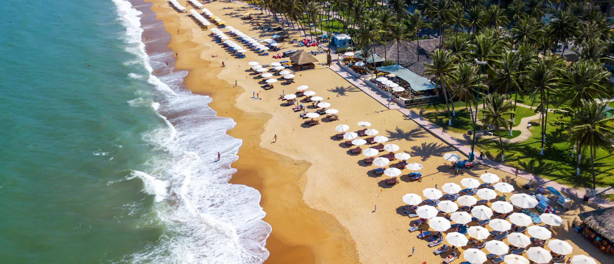 Aerial view of An Bang Beach in Hoi An, with white umbrellas, sun loungers, and turquoise waves.