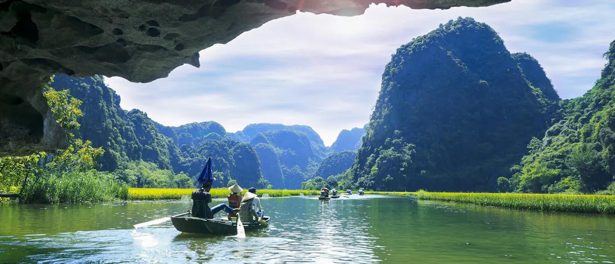 People in boats navigate the tranquil green waters of Tam Coc, framed by majestic limestone karsts.